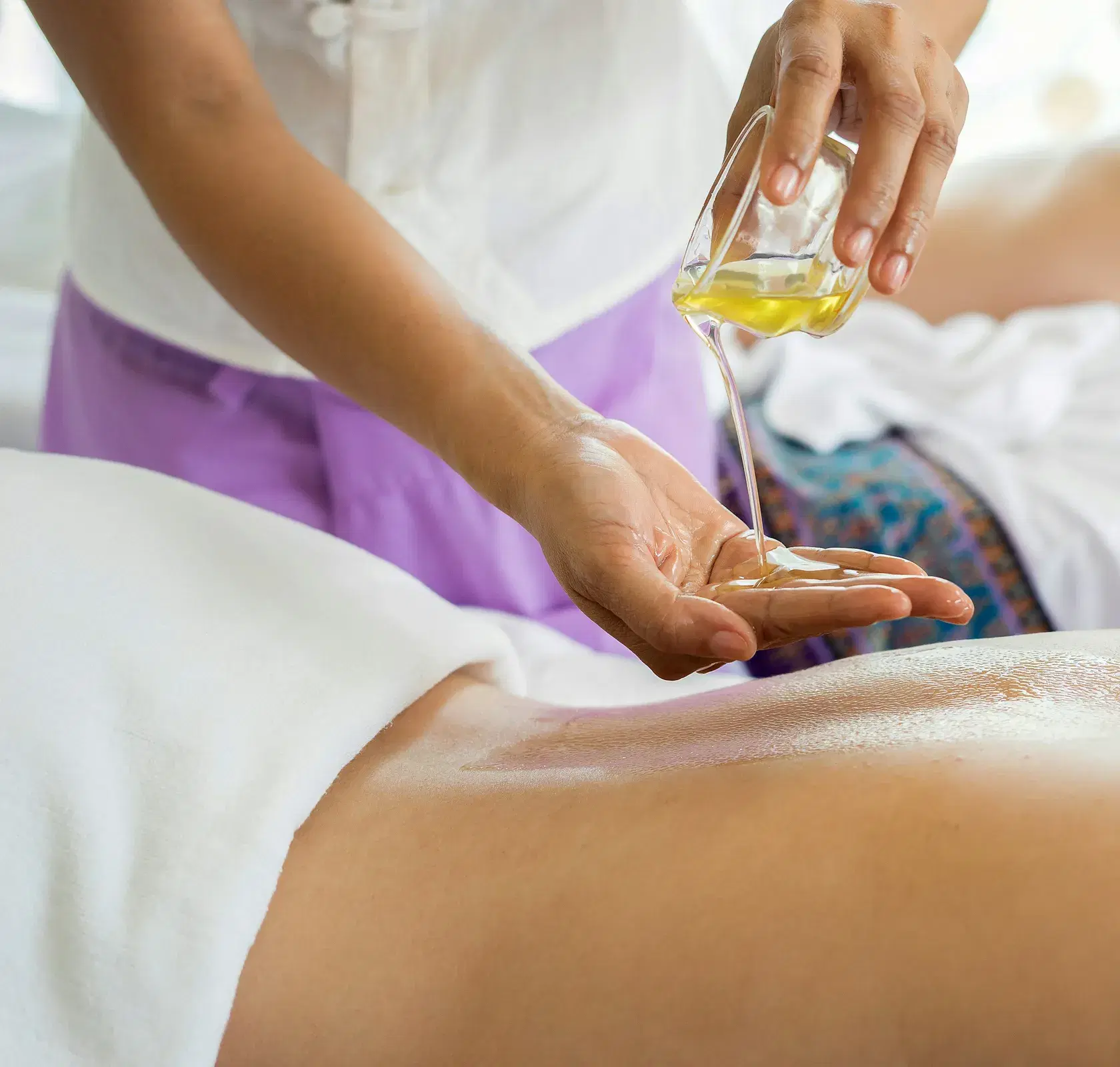 Massage oil being poured into a therapist’s hand above a person’s back