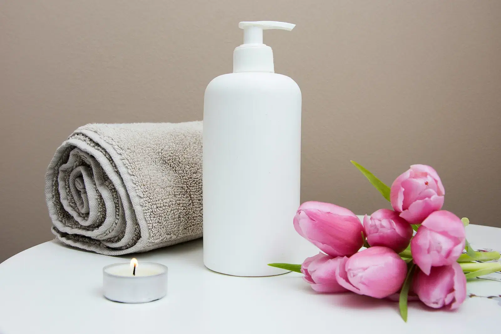A spa towel, lotion bottle and pink tulips on a treatment table